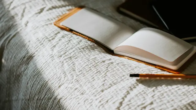 Open journal and pencil on a cozy bed, symbolizing a peaceful morning journaling routine for women