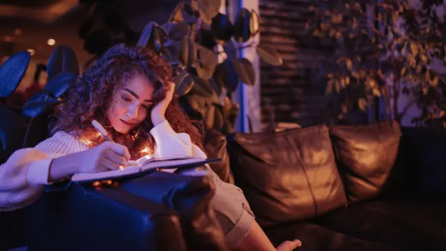 Woman writing in her journal during the evening, surrounded by warm light — part of her self-care and reflection routine.