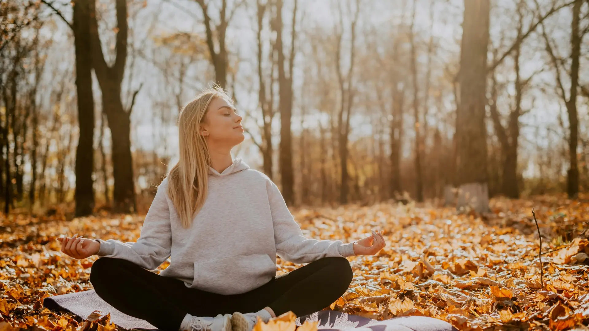 Woman meditating outdoors surrounded by autumn leaves, finding stillness in a busy world