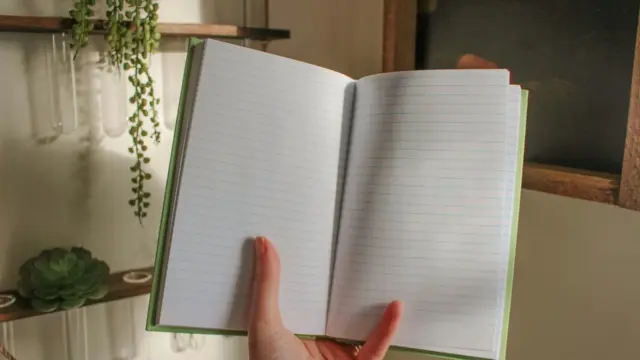 A person holding an open blank lined journal in warm natural light, ready for gratitude journaling.