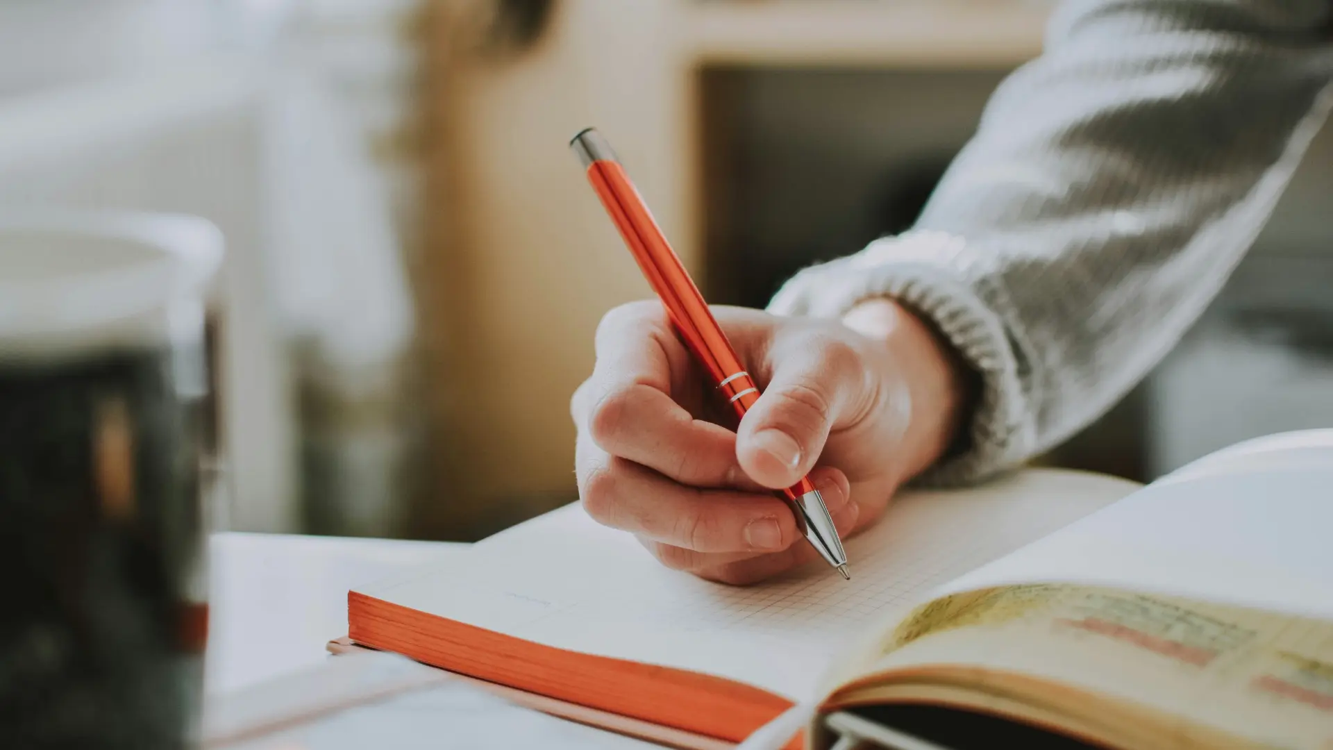 Person writing in a gratitude journal with a red pen during a mindful daily reflection routine.