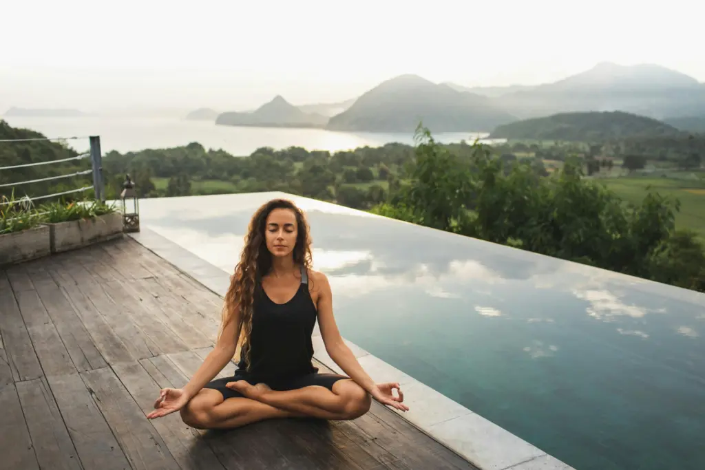 Woman meditating by a calm pool overlooking mountains, symbolizing balance and inner peace