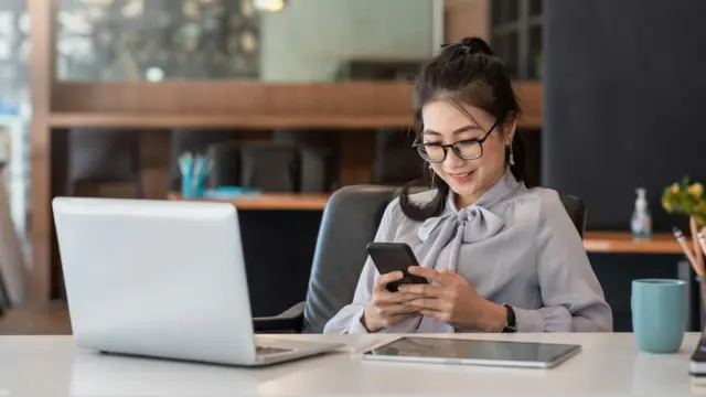 Woman smiling while checking her phone at work, representing mindful and balanced digital habits.