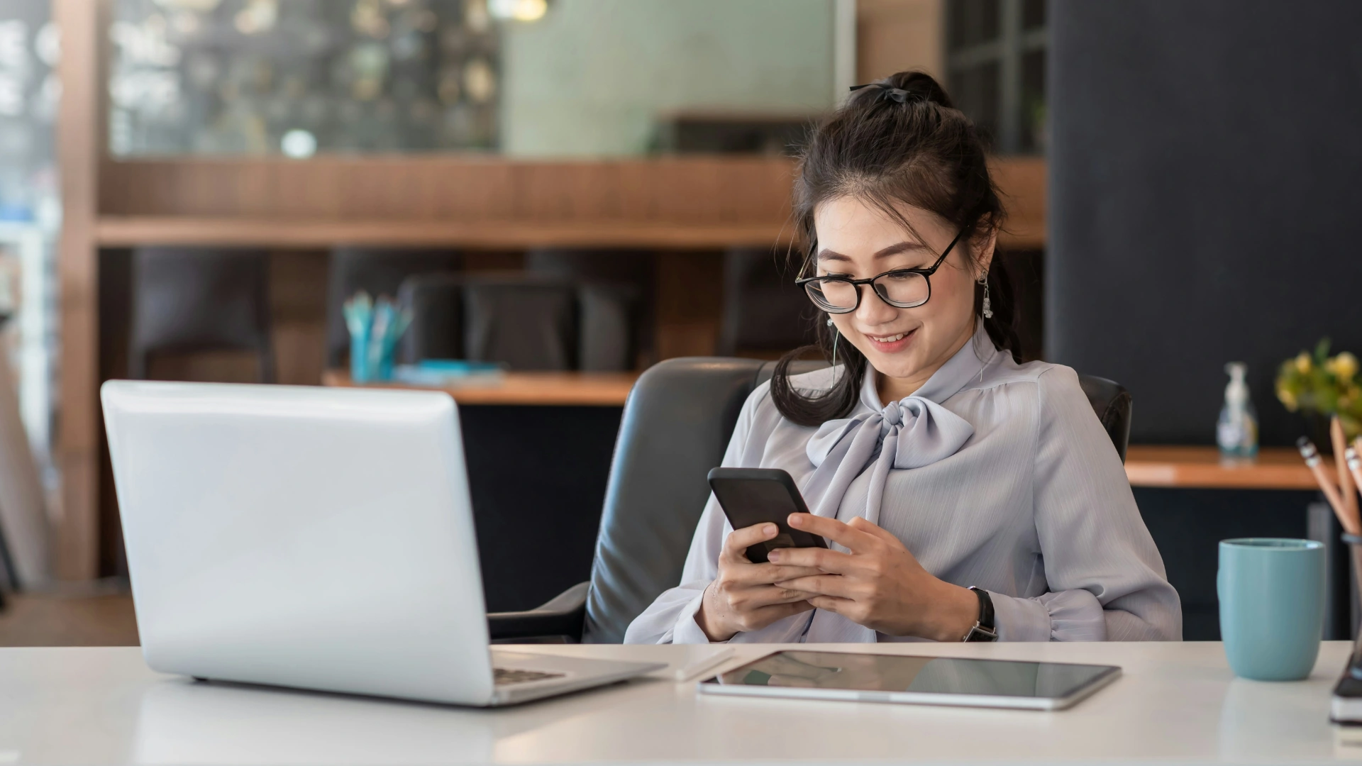 Woman smiling while checking her phone at work, representing mindful and balanced digital habits.