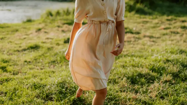 Woman walking barefoot in the grass, symbolizing mindfulness and the art of slowing down.