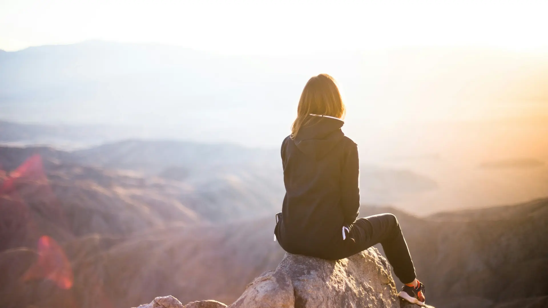 Woman sitting on a mountain at sunrise, reflecting and finding confidence after self-doubt