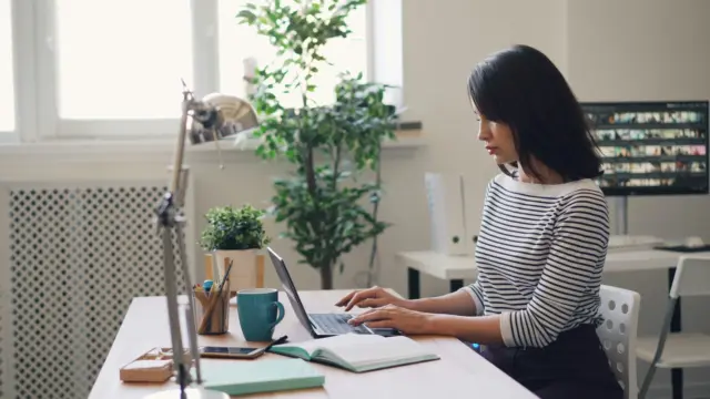 Woman organizing her week on a laptop with a journal and coffee cup on the desk, representing focus and clarity during a weekly reset.
