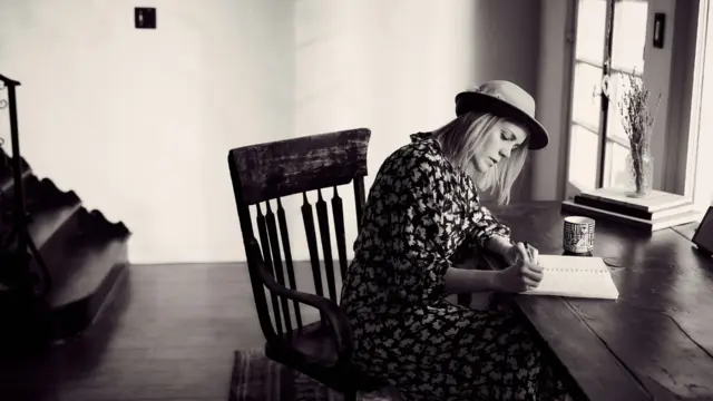 Woman writing intentions in a journal at a cozy wooden desk, representing mindful daily practice