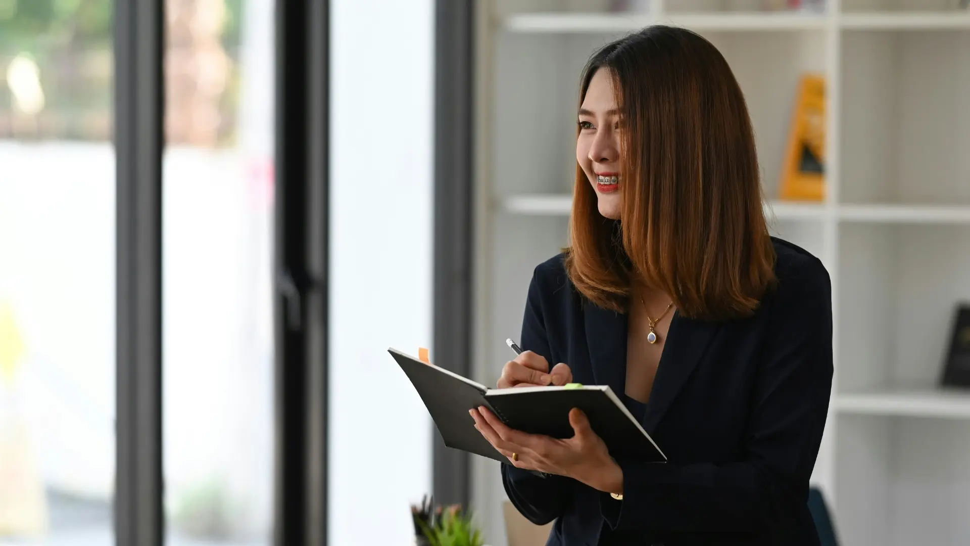 Professional woman smiling while writing in a journal during a team meeting in a modern office.