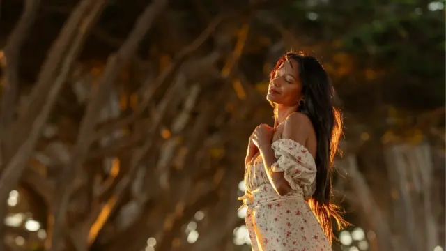 Woman standing in golden evening light, eyes closed in peaceful gratitude and reflection.