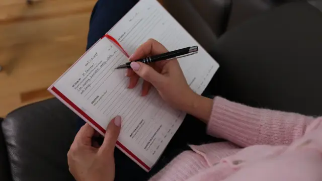 Person writing daily goals in the iAmEvolving Journal, focusing on goal setting and gratitude.