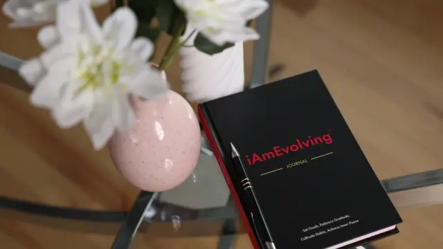 The iAmEvolving Journal placed beside flowers and a pen — a calm space for daily gratitude practice.