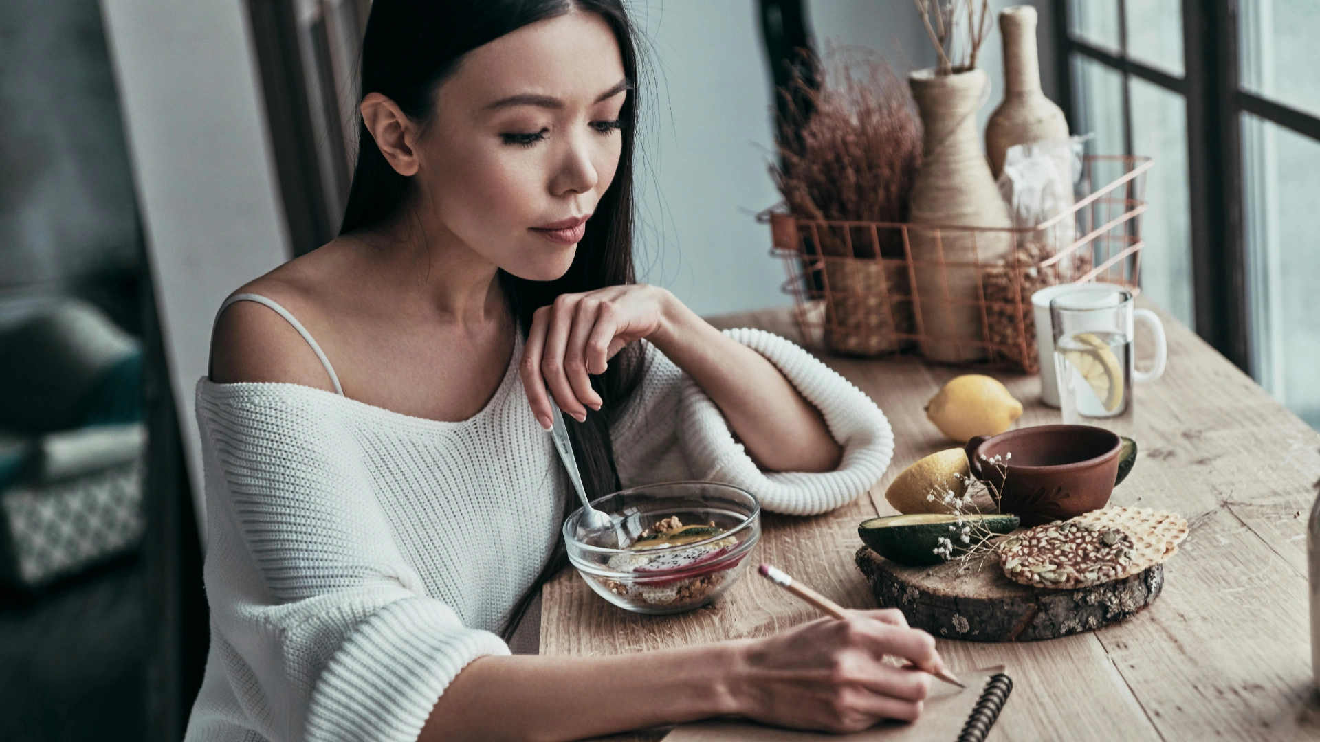Person journaling mindfully by the window with morning light and tea, symbolizing awareness and daily habit reflection.