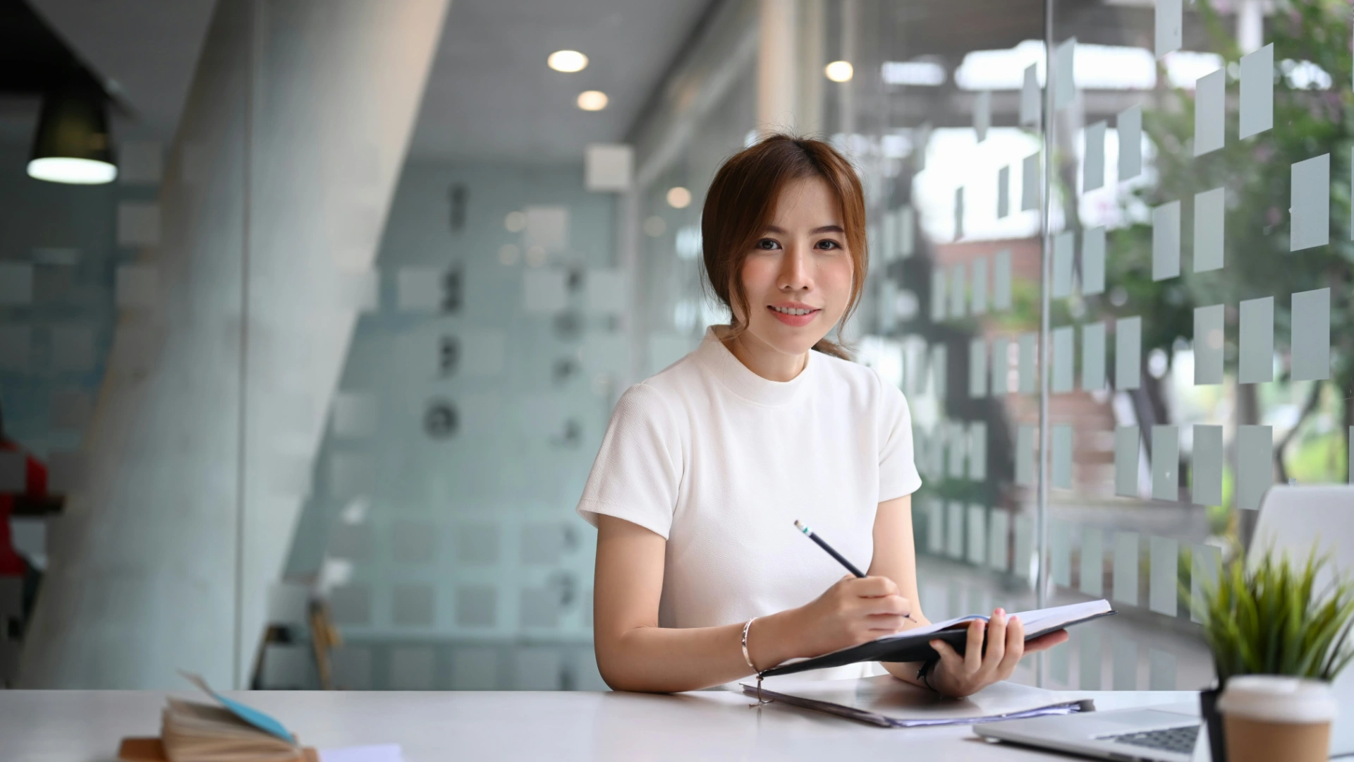 Woman writing in a notebook in a bright, calm workspace — symbolizing mindful consistency and balance.