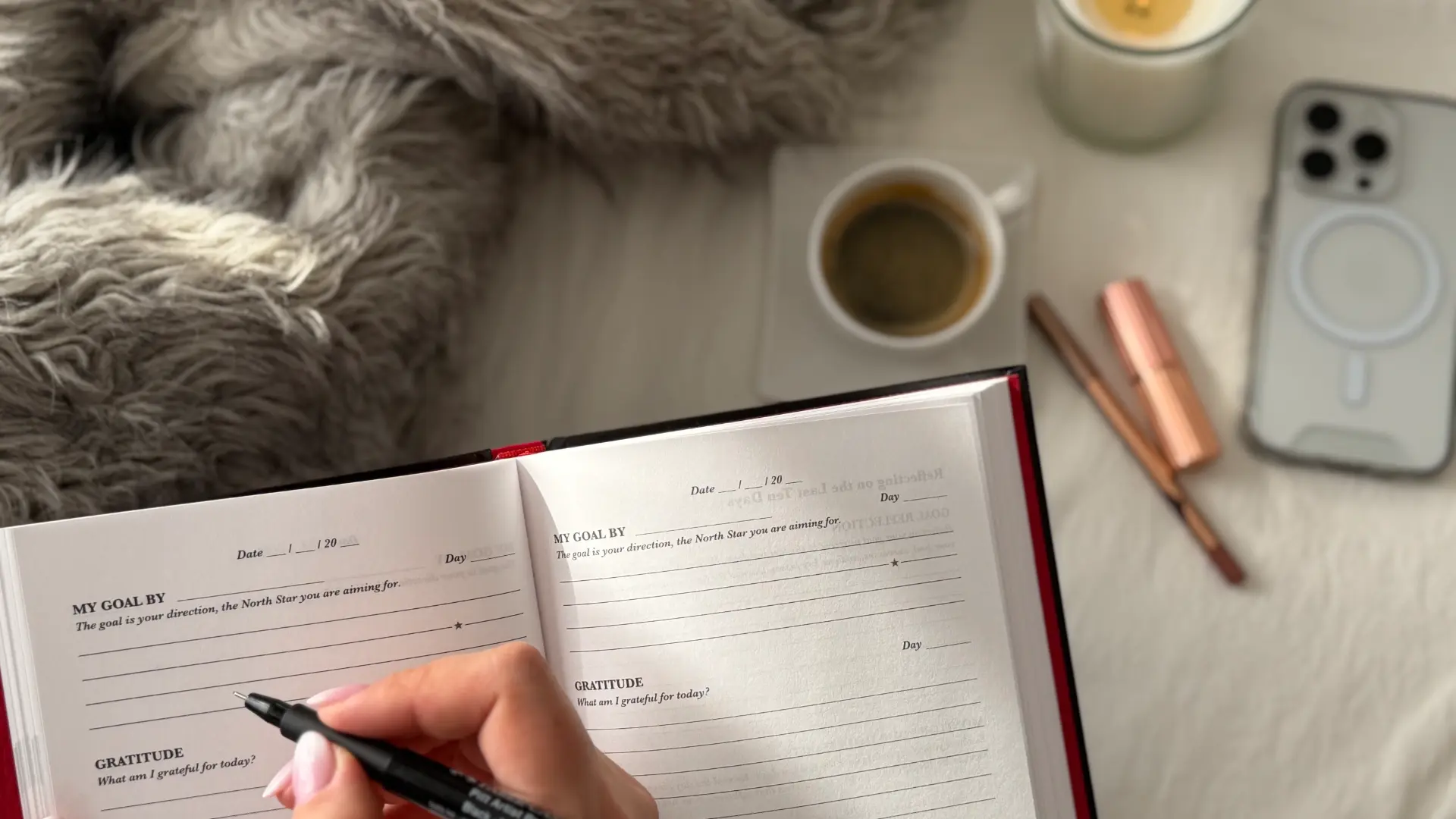 Person writing in the iAmEvolving Journal with coffee and candle nearby, reflecting on thoughts and practicing mindfulness.