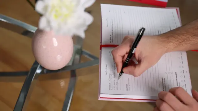 Person writing in the iAmEvolving Journal while setting daily goals at a glass table