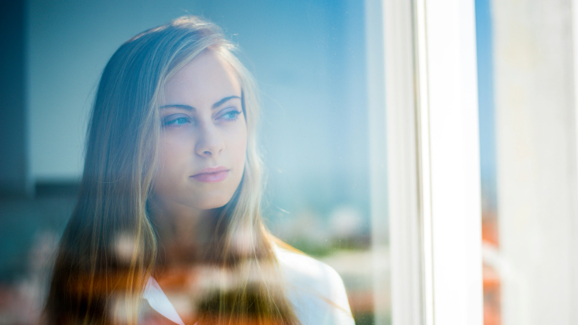 Woman looking out a window in a quiet moment, reflecting feelings of anxiety and anticipation