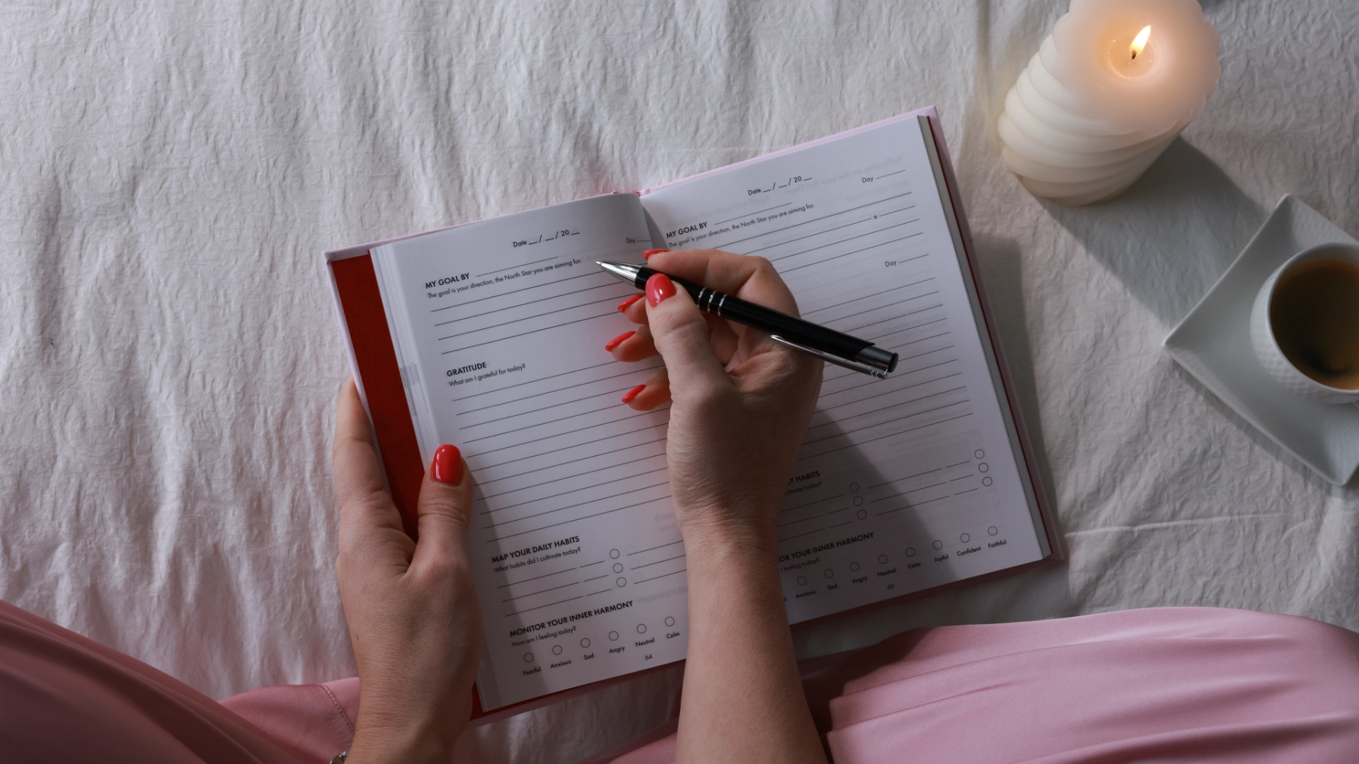 Person holding a pen ready to write in the iAmEvolving Journal daily page with a candle nearby as a practice for calming an overthinking mind