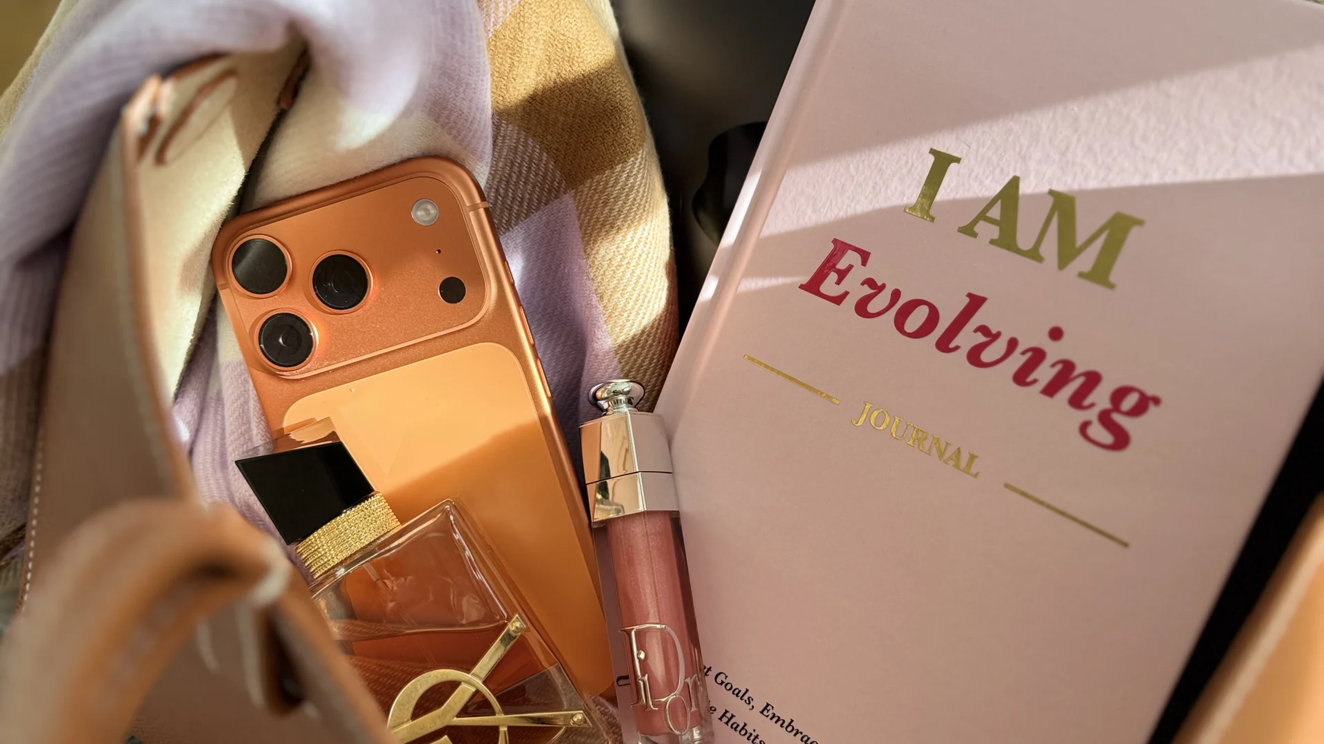 iAmEvolving Journal in pink with Dior perfume, lip gloss, phone, and scarf — a lifestyle flat lay for personal growth journaling