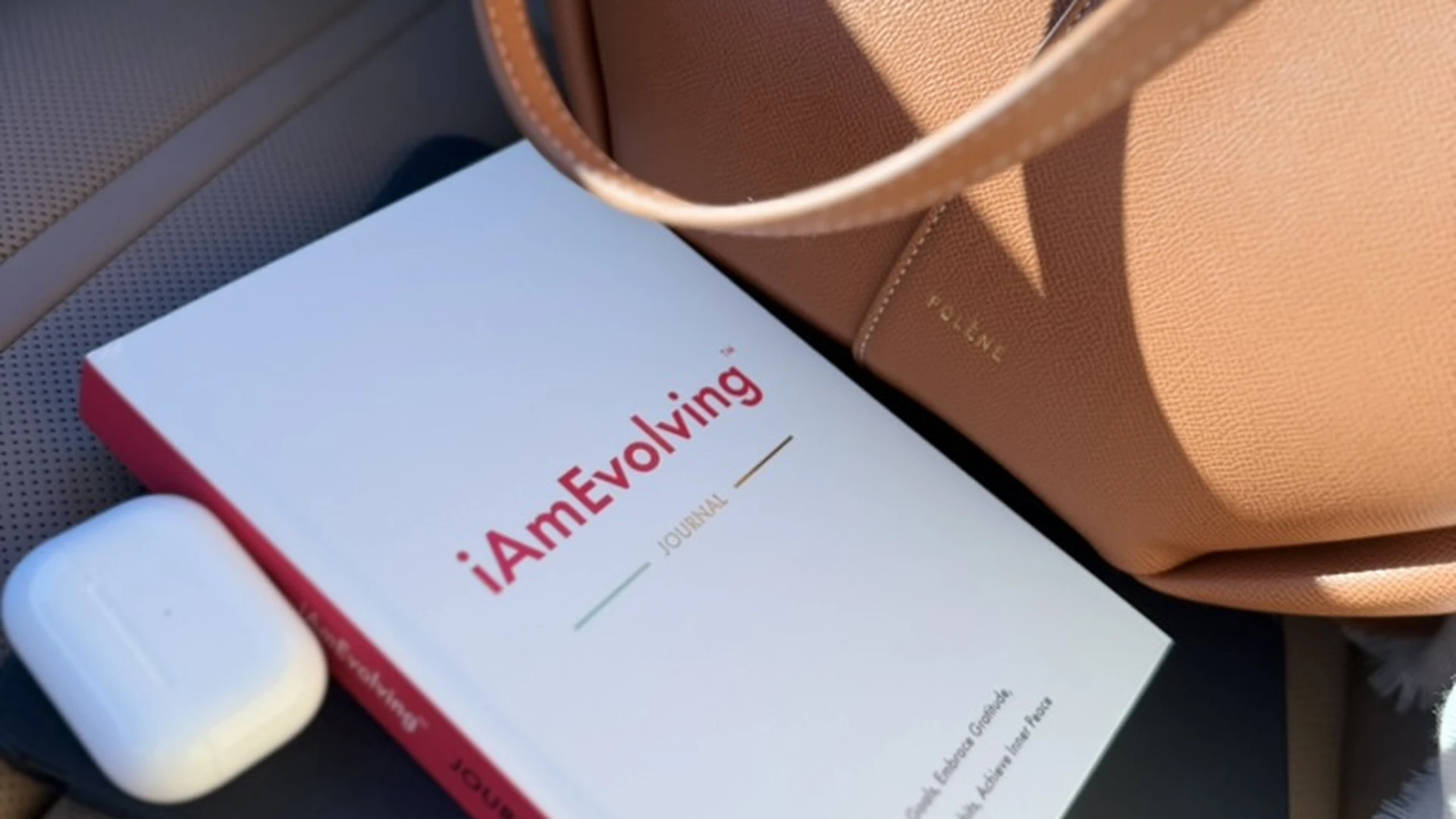 iAmEvolving Journal with leather bag and AirPods on a car seat — best journals to start in spring