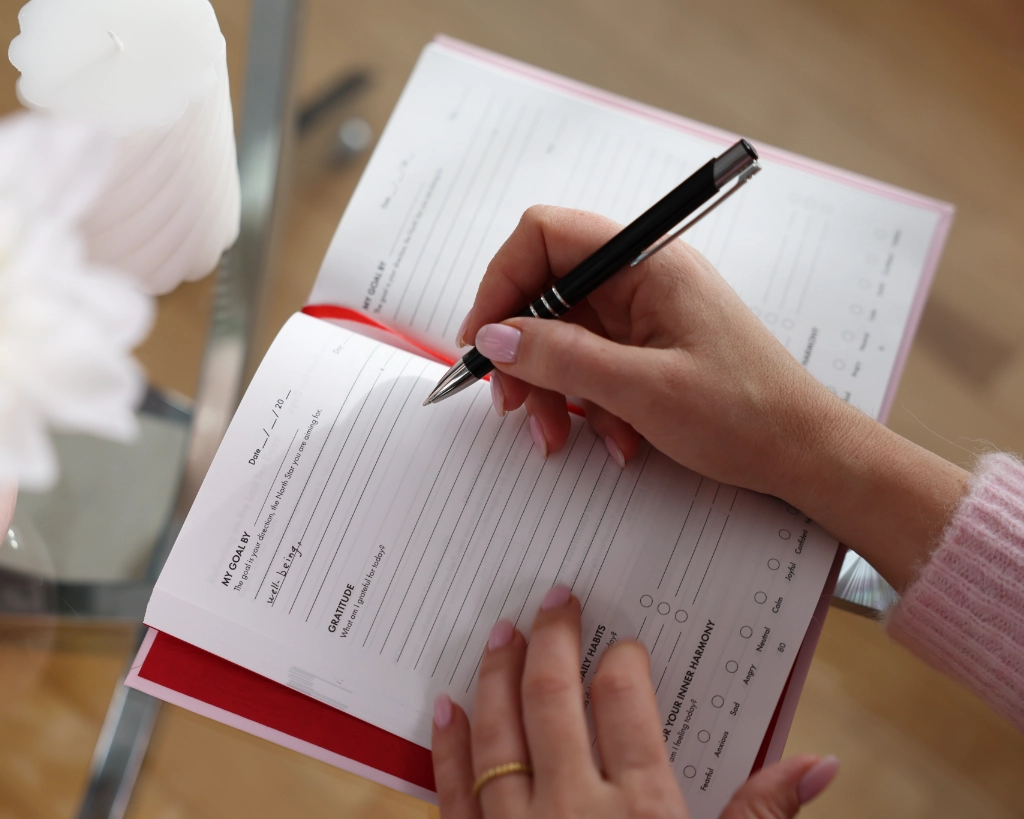 Woman holding the iAmEvolving Journal open to a daily page showing goal setting, gratitude, habits, and inner harmony prompts